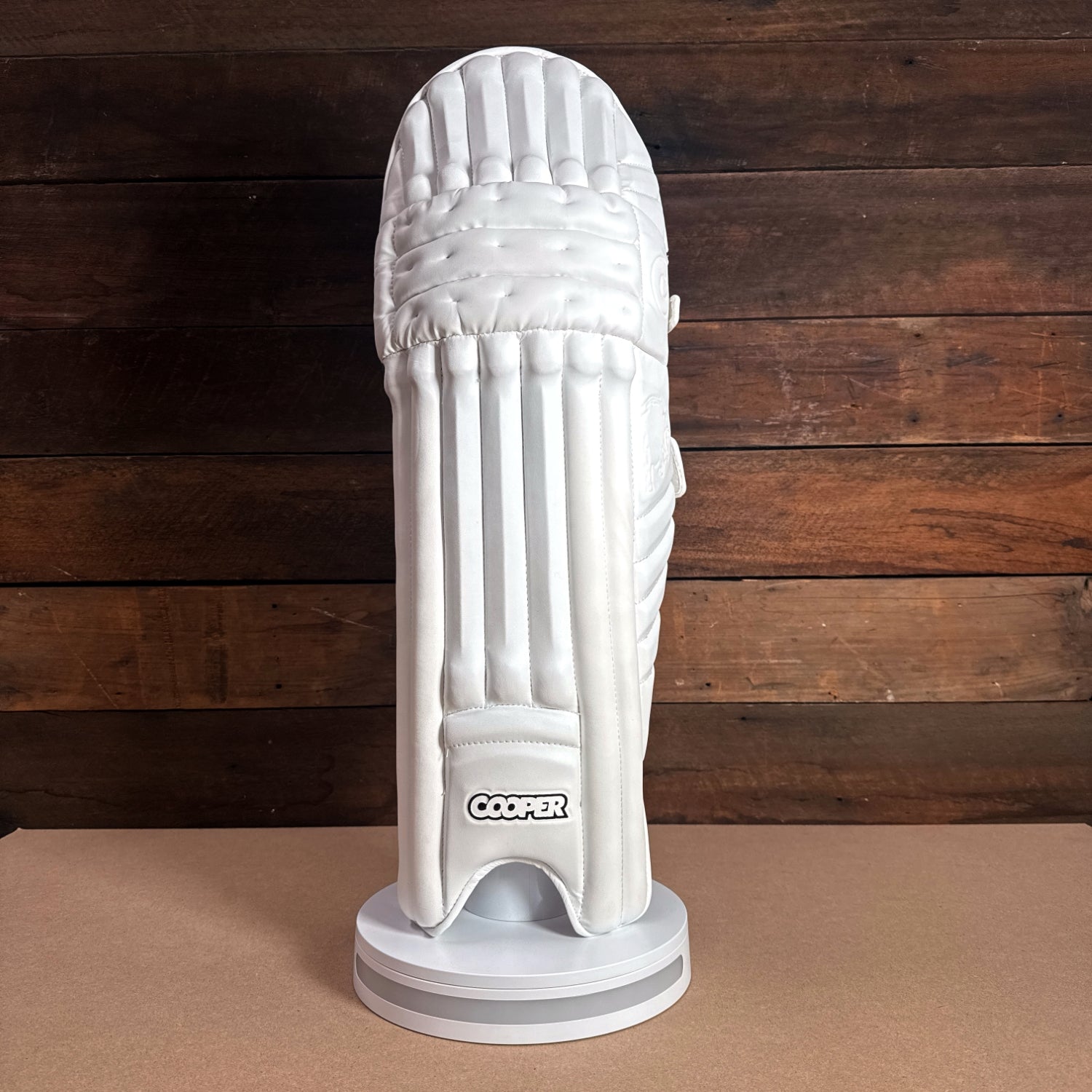 Cooper cricket pad displayed on a stand, showcasing its sleek design and premium white material.