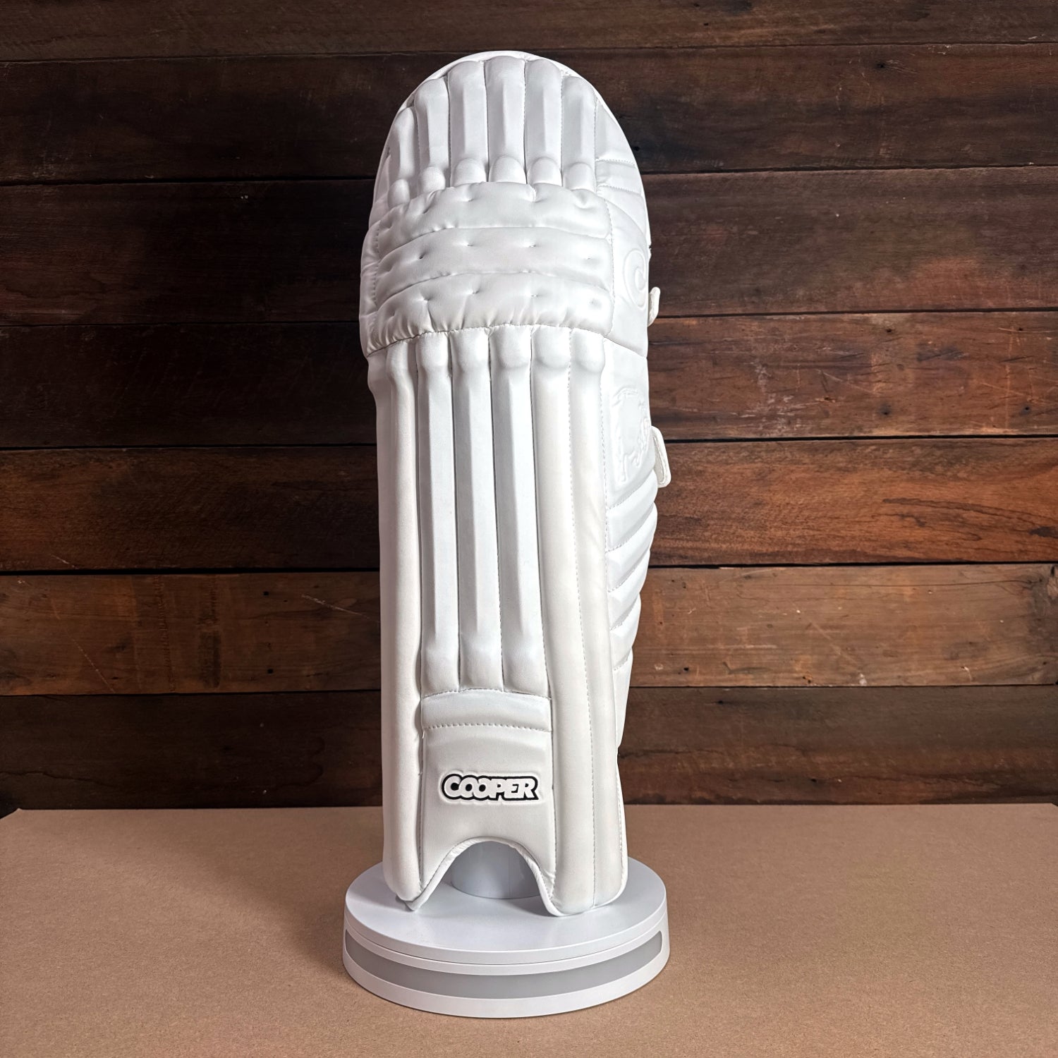 White Cooper cricket pad displayed on a stand, showcasing its premium design and protection features.