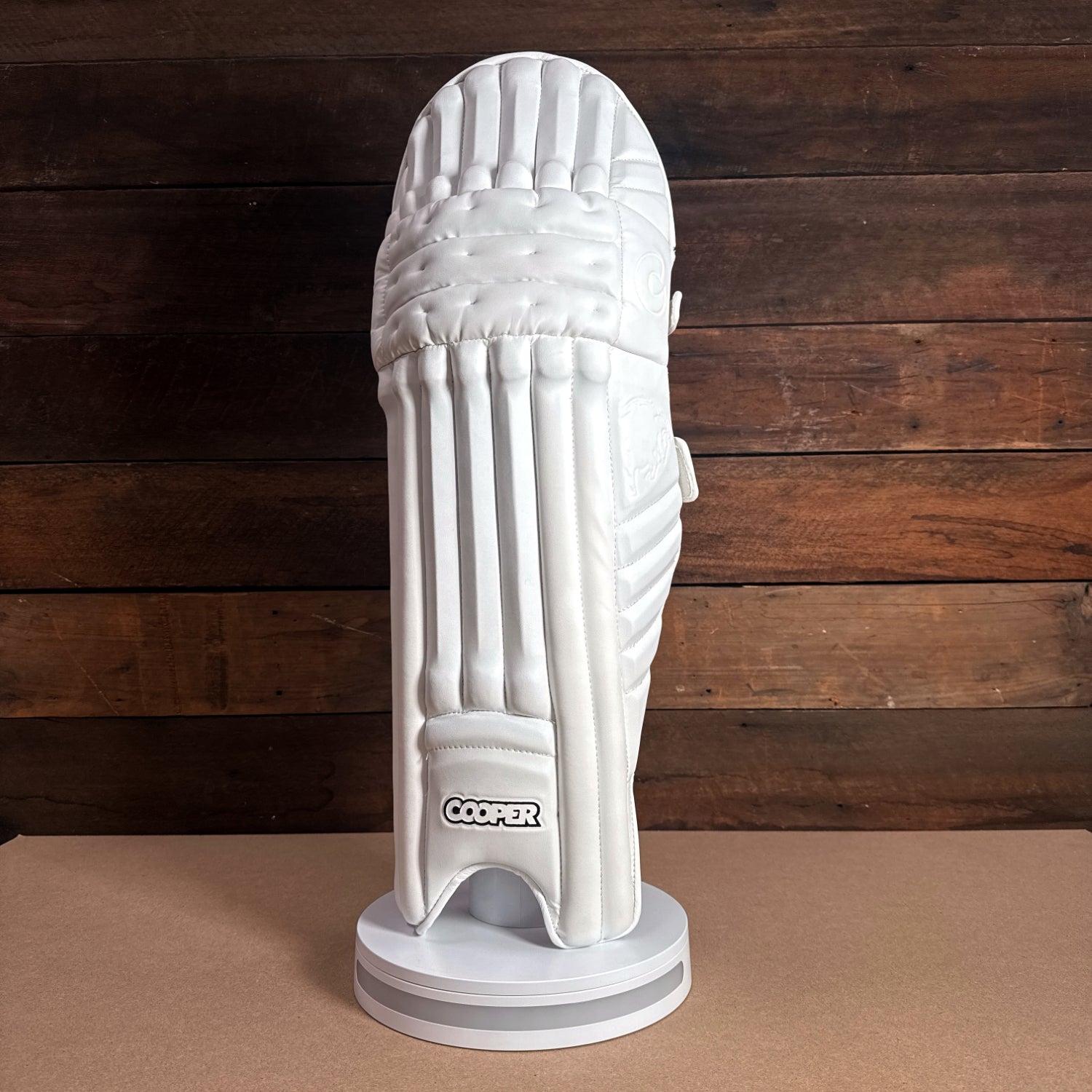 Cooper cricket batting pad displayed on a stand, showcasing its sleek white design and protective features.