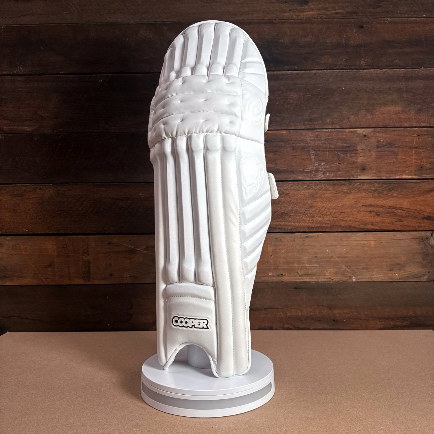 Cooper cricket pad displayed on a stand, featuring a sleek white design and premium padding for protection.