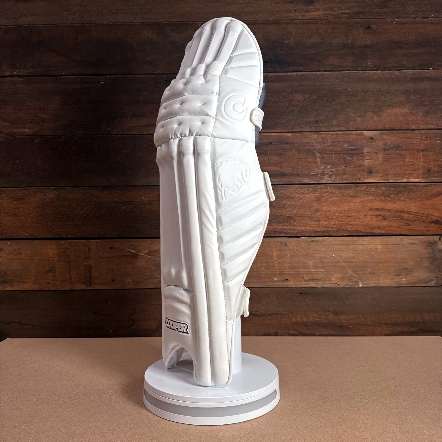 Cooper cricket pads displayed on a stand, featuring a sleek white design and premium protective features.
