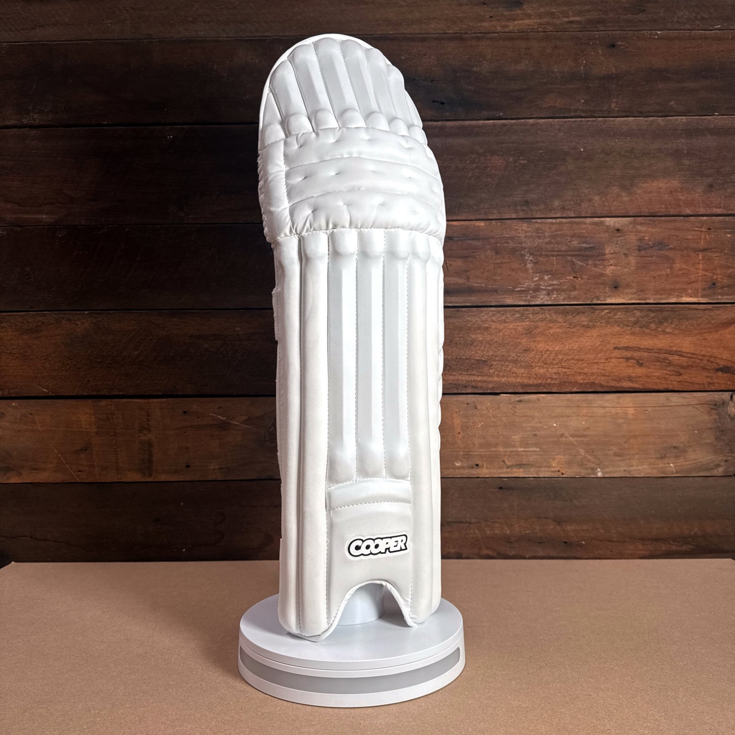 Cooper cricket pad displayed on a pedestal, featuring a sleek white design and protective grooves.
