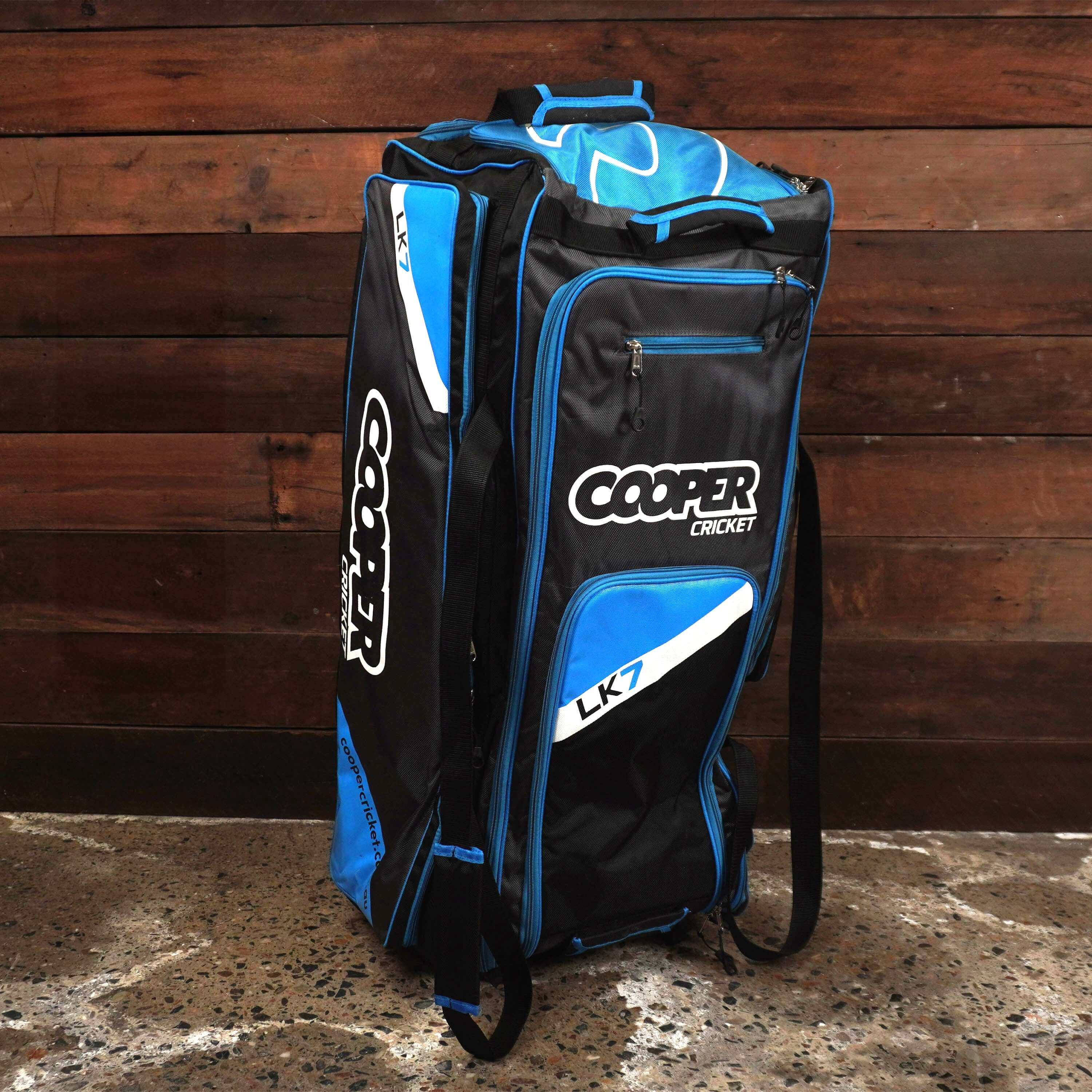 "LK7 cricket bag with multiple compartments for gear, shown in black and blue design against wooden background"