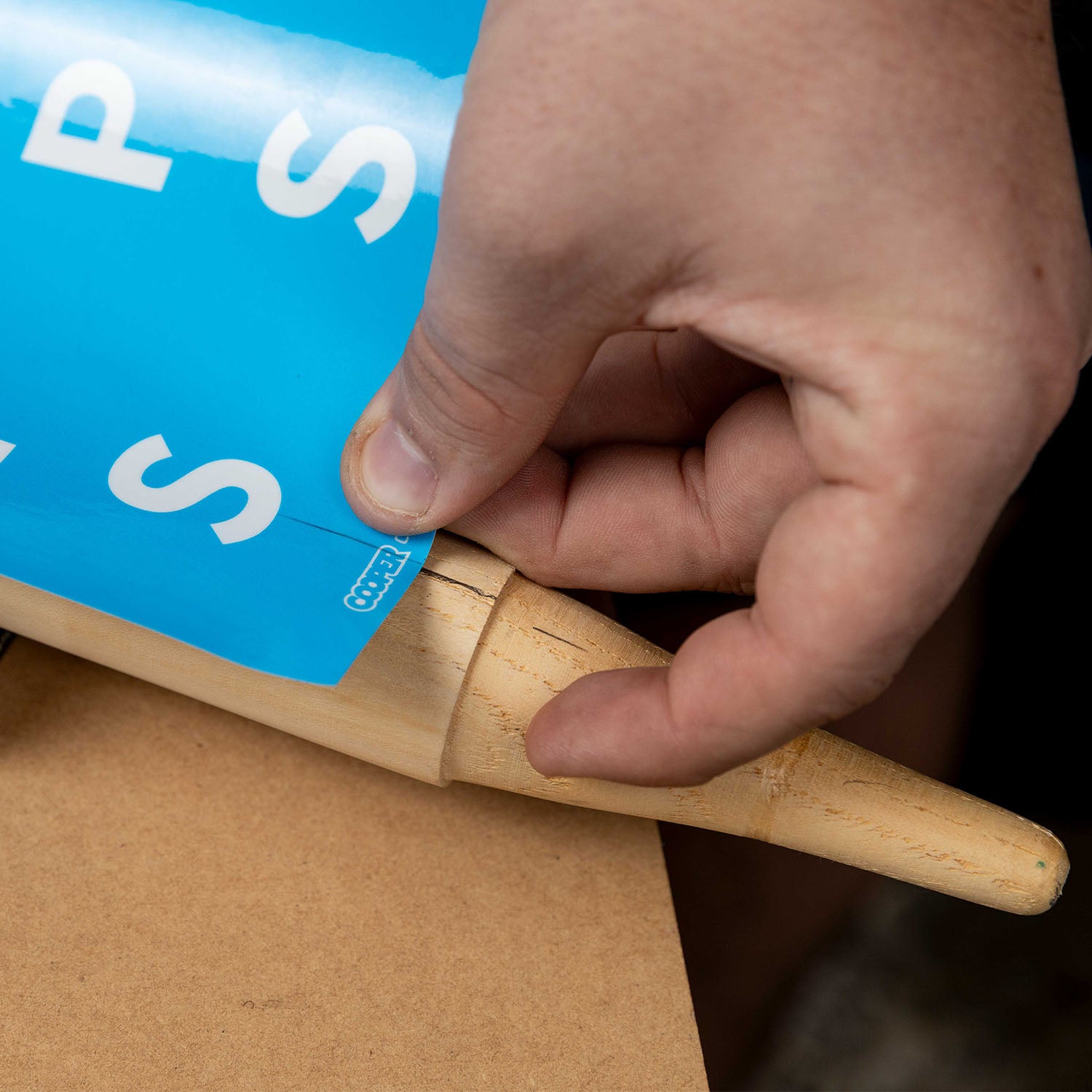 Applying cricket stump sticker with a marker tool for precise alignment on wooden stump.