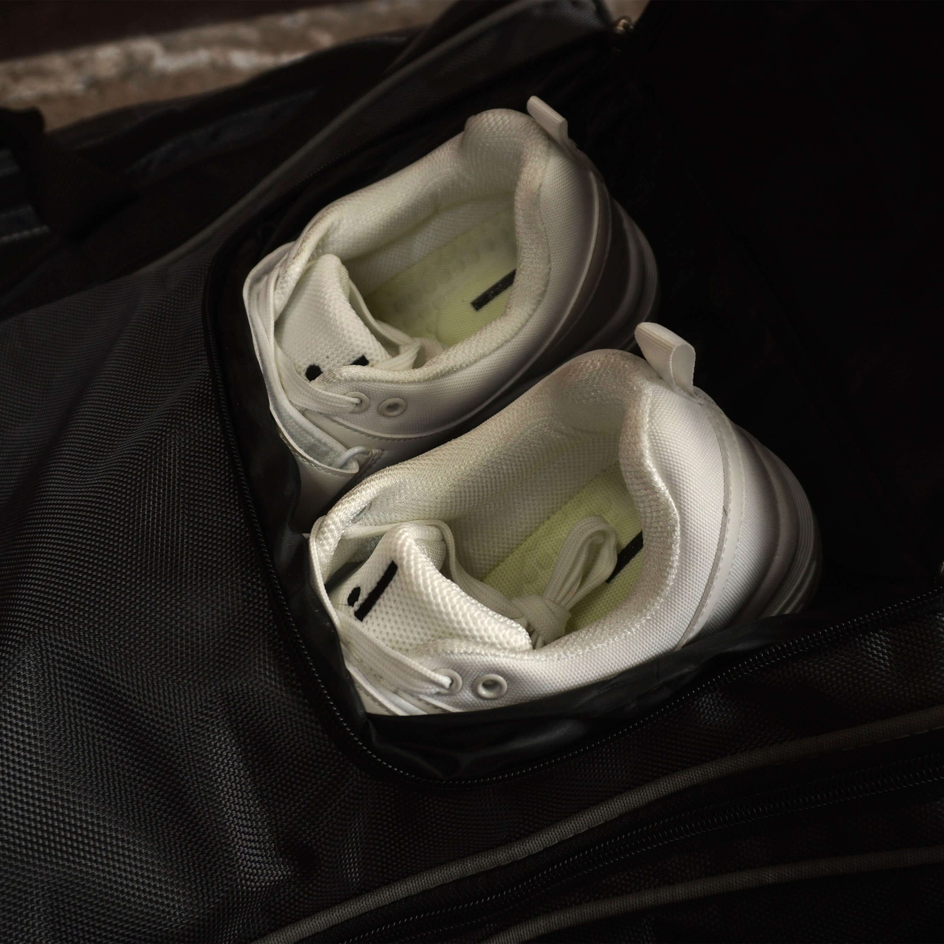Pair of white shoes stored inside a black LX9 cricket bag compartment.