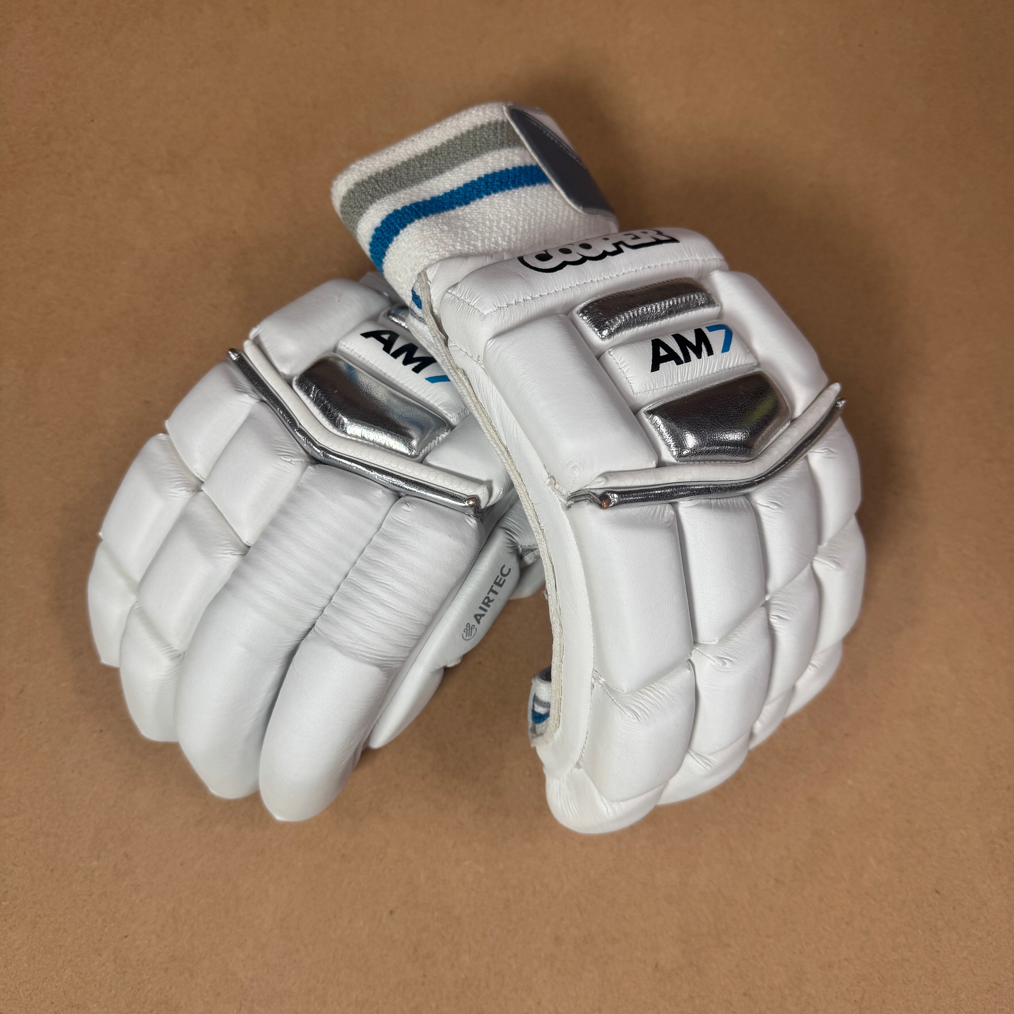 AM7 gloves with premium sheep leather, split construction for comfort, AIRTEC ventilation, and dual-sided sweatbands on a brown background.