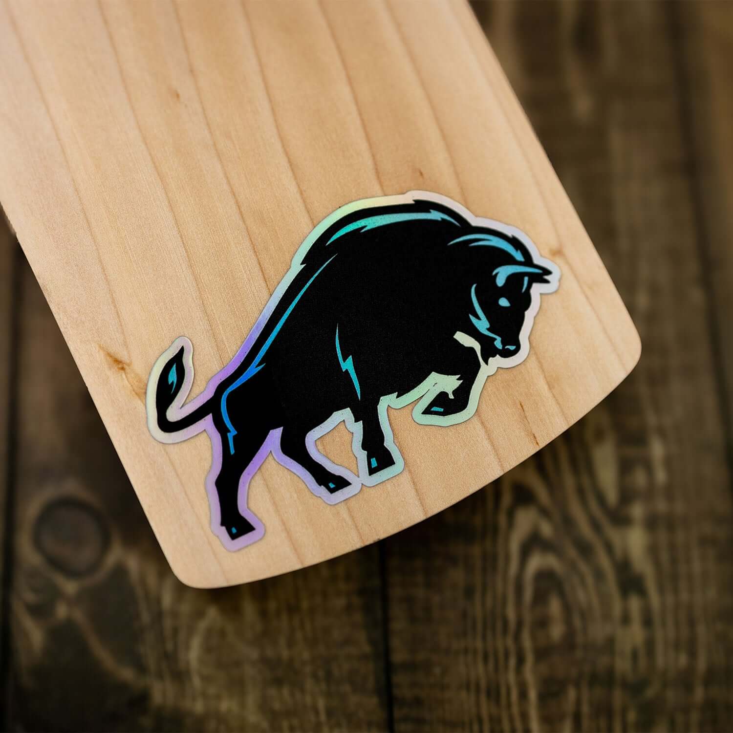 Close-up of a black bull sticker on a cricket bat, showcasing a sleek design on wooden texture.