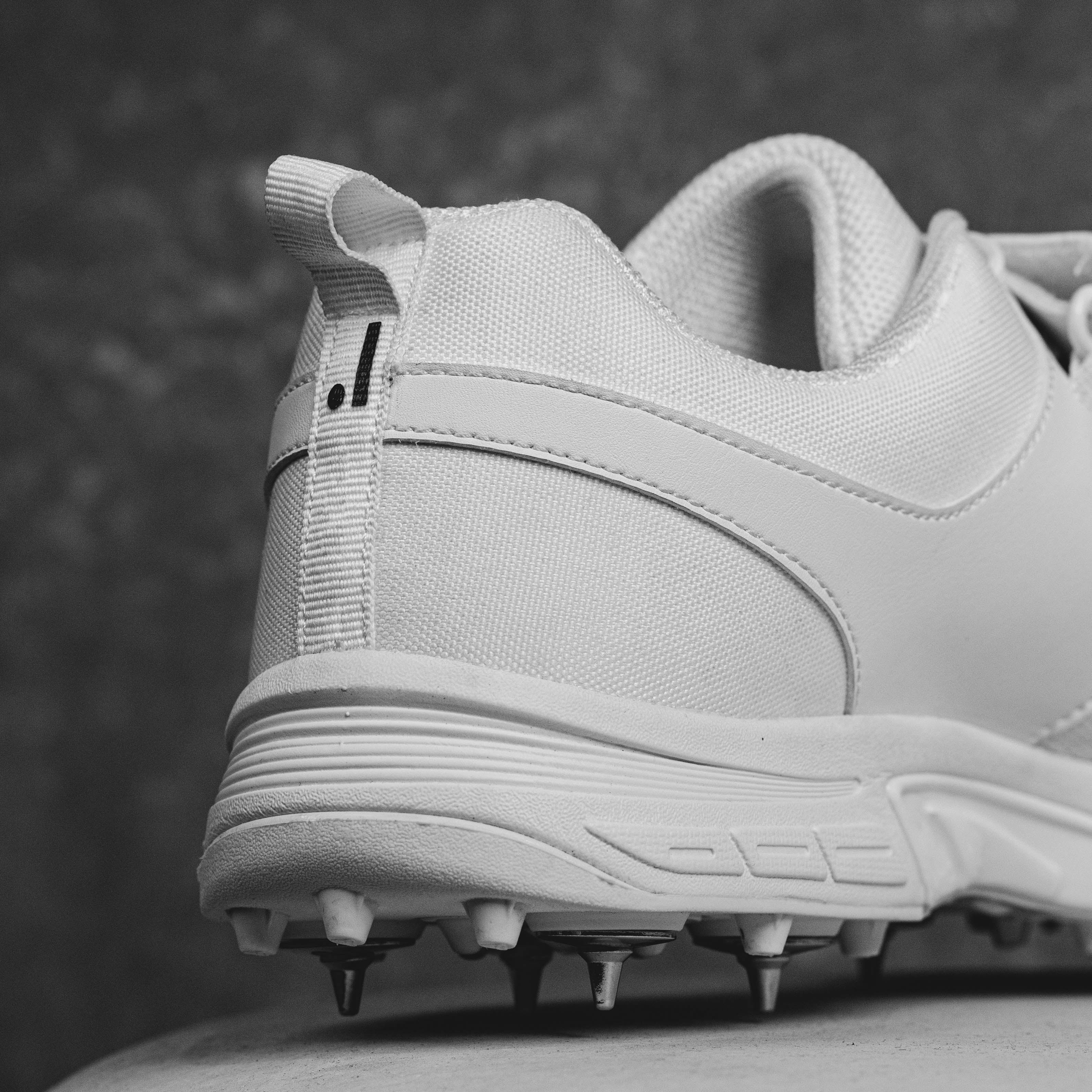 Close-up of white IDONEUS ID1 Cricket Shoes with steel spikes for superior grip and durability in sports activities.