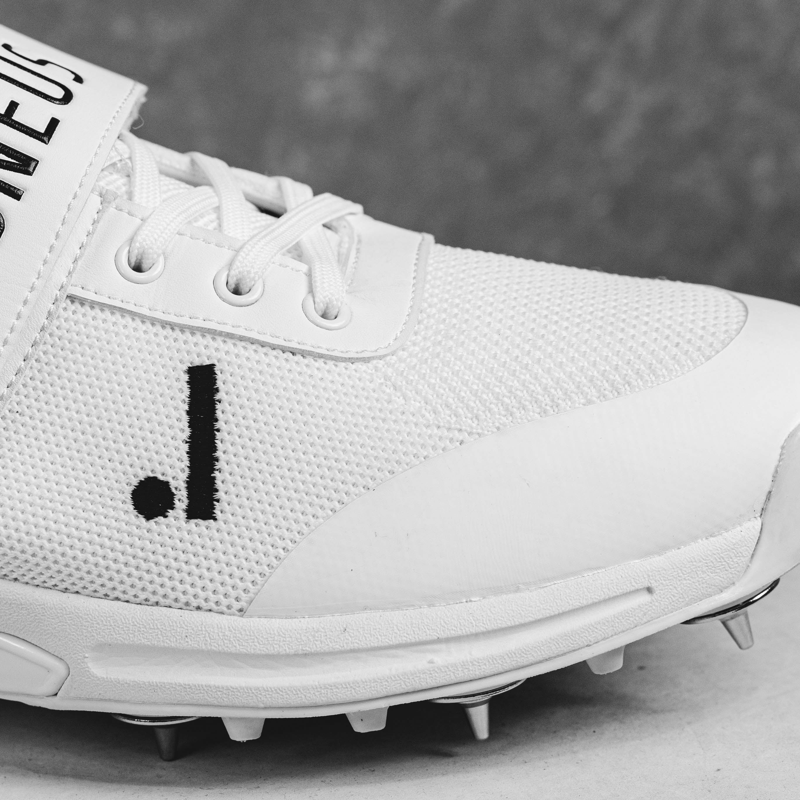 White IDONEUS ID1 cricket shoe with steel spikes for superior grip and stability on various surfaces.