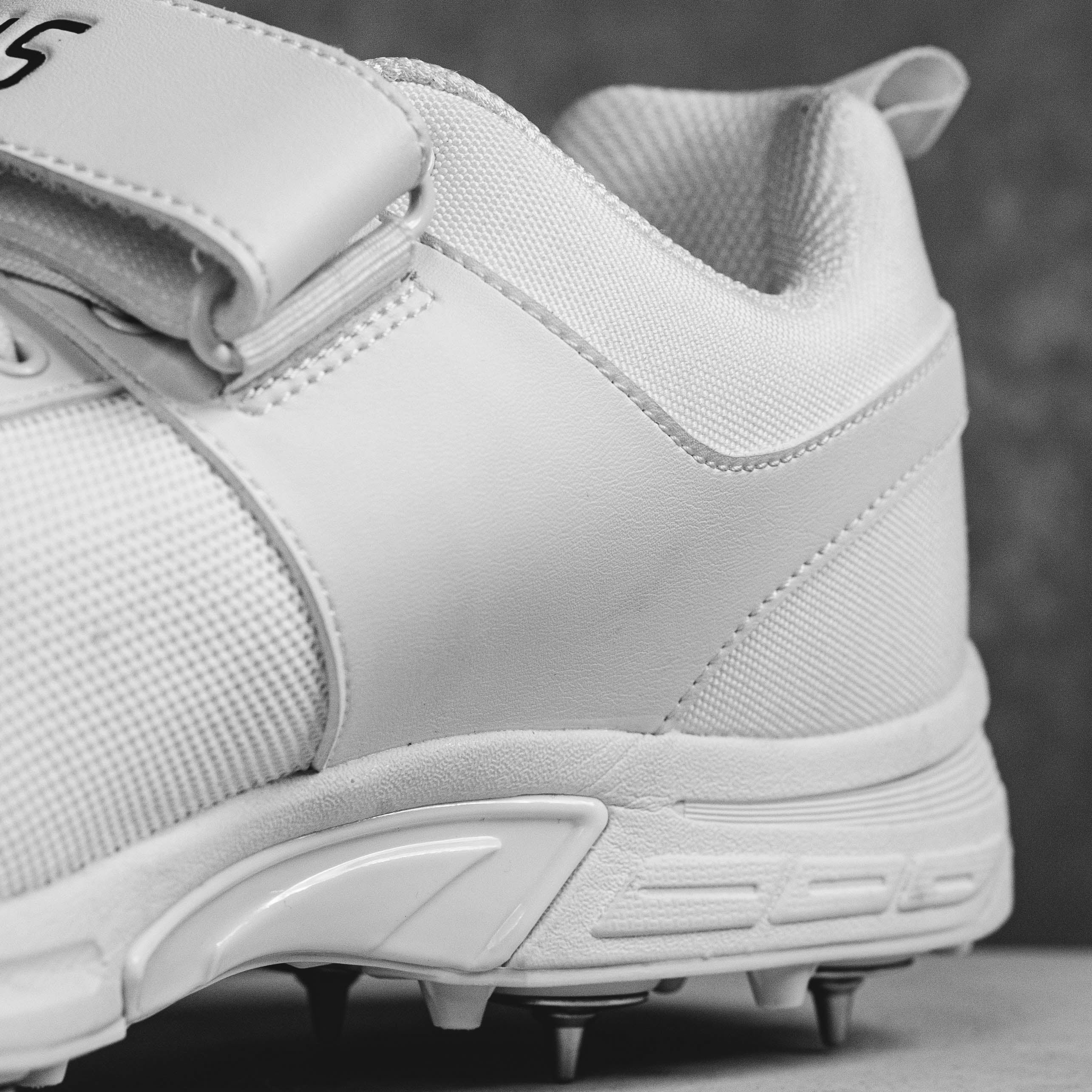 Close-up of white IDONEUS ID1 cricket shoe with steel spikes for superior grip and durability.